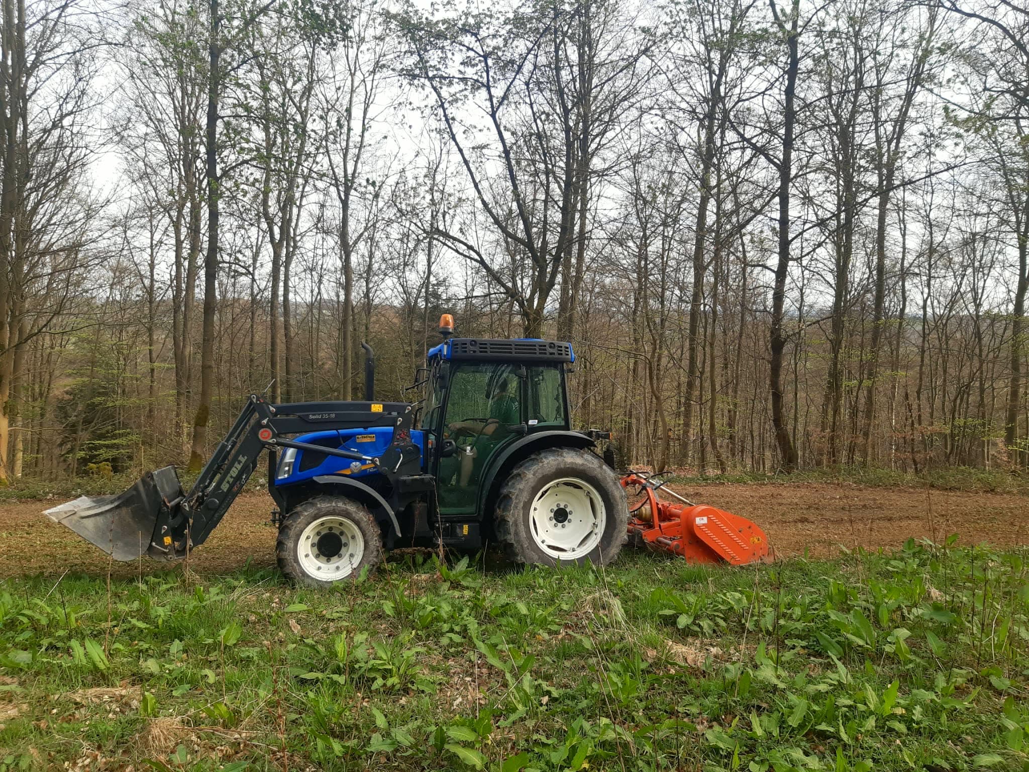 Traktor mit Mulcher auf einer Wildwiese am Waldrand